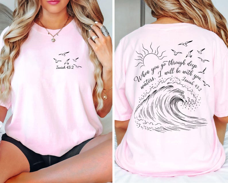 May include: A light pink t-shirt with a black graphic of birds and the text "Isaiah 43:2" on the front. The back features a sun, birds, a wave, and the quote "When you go through deep waters, I will be with you. Isaiah 43:2."