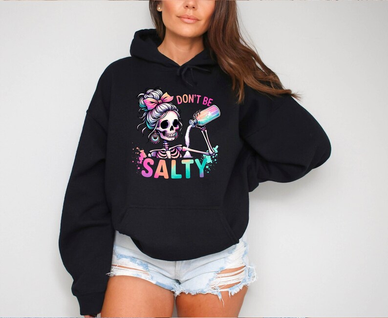 May include: Black hoodie with a colorful graphic of a skeleton with a bun in her hair pouring a drink from a bottle. The text "Don't be Salty" is printed below the graphic.