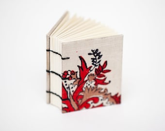 Mini cuaderno de tela gruesa roja, dorada y negra con encuadernación copta.