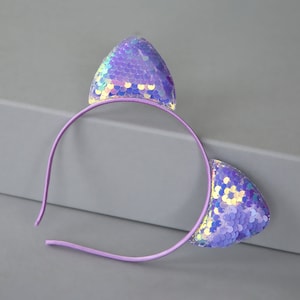 May include: Purple headband with iridescent sequin cat ears. The headband is made of plastic and the ears are made of fabric.