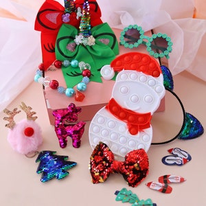 May include: A Christmas-themed gift box filled with various items, including a red and green bow, a snowman pop-it toy, a pink reindeer keyring, a red and green sequin bow, and a blue and green sequin Christmas tree.