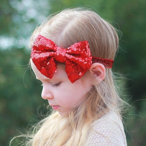 Puede incluir: Una niña pequeña con el pelo largo y rubio que lleva una diadema roja con un lazo de lentejuelas.