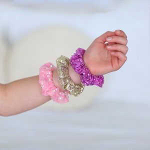 May include: Three sequined hair scrunchies in pink, gold, and purple.