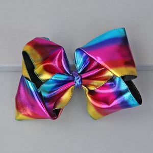 May include: A large, colorful hair bow with a metallic sheen. The bow features a gradient of colors, including yellow, pink, blue, and purple. The bow is made of a shiny material and has a black backing.