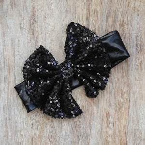 May include: Black sequined bow headband with a black elastic band. The bow is large and has a layered design.