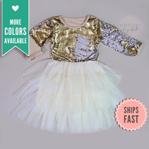 Könnte beinhalten: Ein gold- und silberfarbenes Paillettenkleid mit langen Ärmeln, cremefarbenem Oberteil und Ärmeln. Der Rock ist aus mehrlagigem, elfenbeinfarbenem Tüll. Der Text "MORE COLORS AVAILABLE" und "SHIPS FAST" ist enthalten.