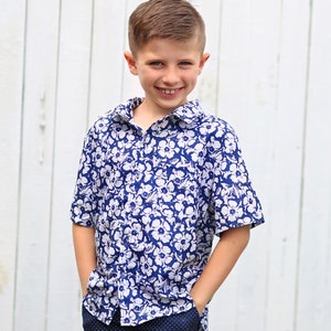 May include: A young boy wearing a blue and white floral short-sleeved shirt and navy blue pants with white polka dots.