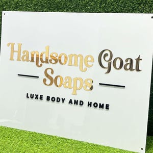 Könnte beinhalten: Weißes Schild mit goldener Aufschrift "Handsome Goat Soaps - Luxe Body and Home".