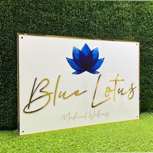 May include: White sign with a gold border and gold lettering. The sign says "Blue Lotus Medical Wellness" with a blue lotus flower graphic above the text.