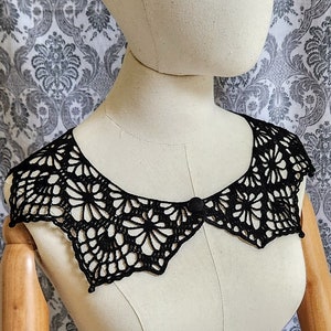 Może przedstawiać: Czarny koronkowy kołnierzyk z ozdobnym guzikiem w środku.