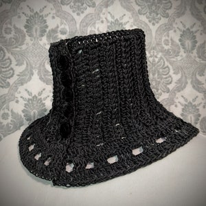 May include: Black crocheted collar with a decorative button detail. The collar has a scalloped edge and is made with a textured stitch.