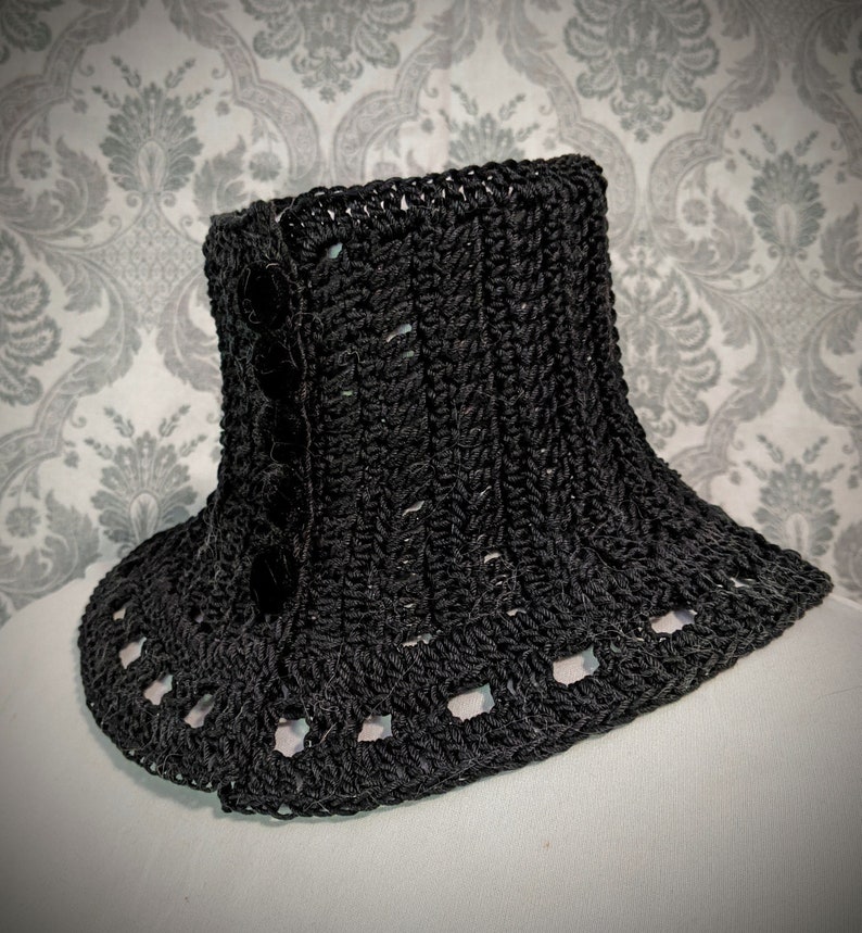 May include: Black crocheted collar with a decorative button detail. The collar has a scalloped edge and is made with a textured stitch.