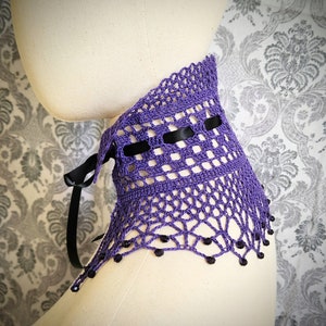 May include: Purple crochet collar with black ribbon and black beads. The collar is on a white mannequin.
