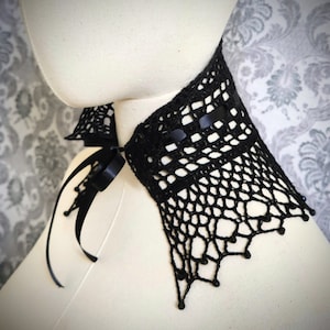 May include: Black crocheted lace choker with a black satin ribbon tie. The choker has a delicate, intricate design and is adorned with small black beads.