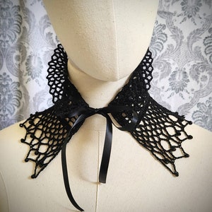 May include: A black crocheted lace collar with a black satin ribbon tie. The collar has a delicate, intricate design and is perfect for adding a touch of elegance to any outfit.