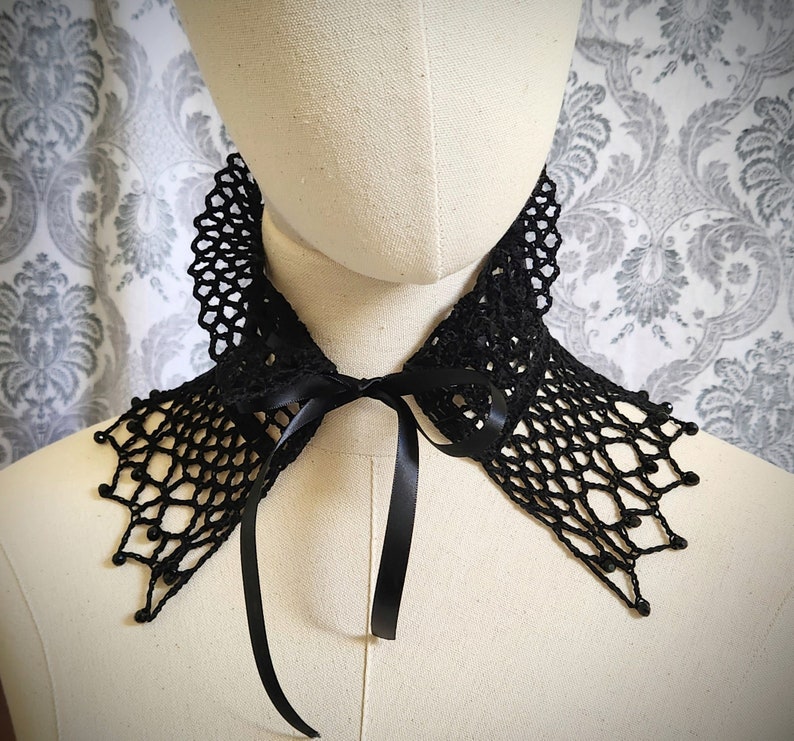 May include: A black crocheted lace collar with a black satin ribbon tie. The collar has a delicate, intricate design and is perfect for adding a touch of elegance to any outfit.