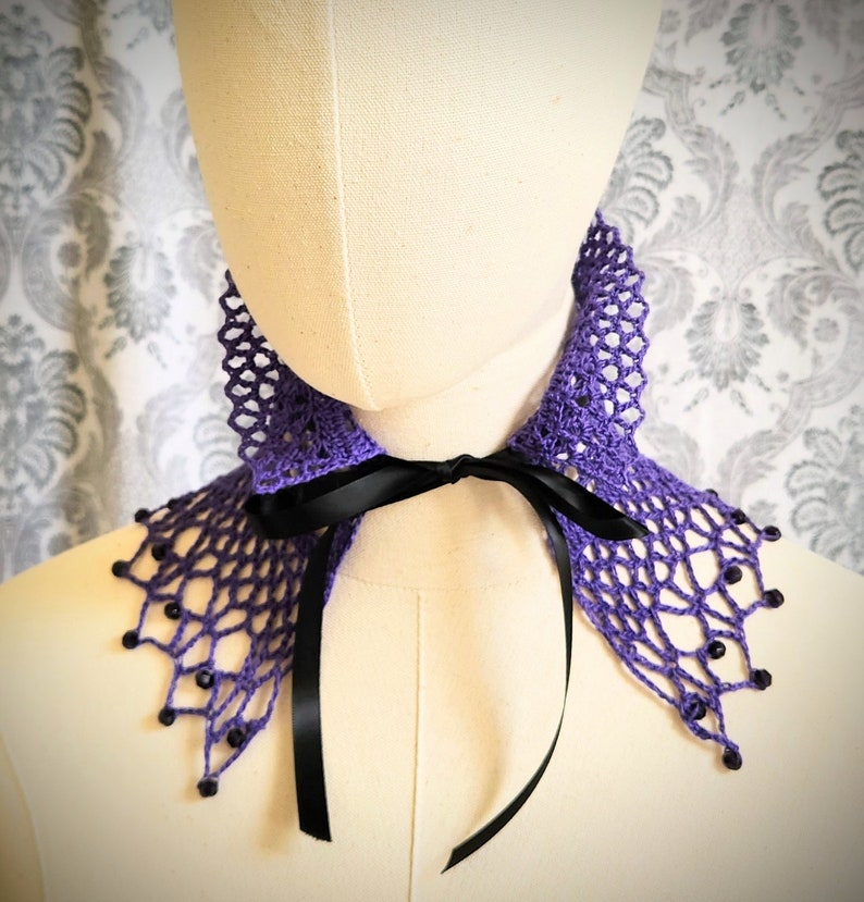May include: Purple crochet collar with black ribbon ties and beaded accents.