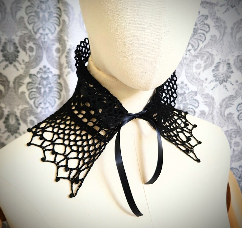 May include: Black crochet collar with a black satin ribbon tie. The collar features a delicate lace pattern and a scalloped edge.