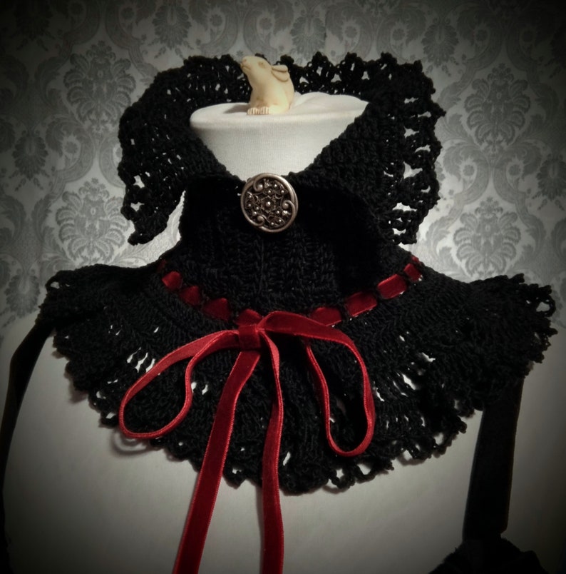 May include: Black crocheted collar with a red velvet ribbon tied in a bow and a silver button in the center.