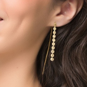 May include: Gold dangle earrings with a chain of small, round discs. The earrings are long and delicate.