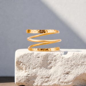 May include: A gold-toned ring featuring a spiral design with three distinct coils. The top and bottom coils exhibit a textured, hammered finish, while the middle coil is smooth and polished, creating a layered appearance in this metal band.