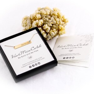 Puede incluir: Un collar de barra de oro con el nombre "kavanagh" grabado. El collar est&aacute; en una caja negra con las palabras "Hot Mix Cold" y "Be Bold and Be Free" en ella. La caja est&aacute; sobre una superficie blanca.