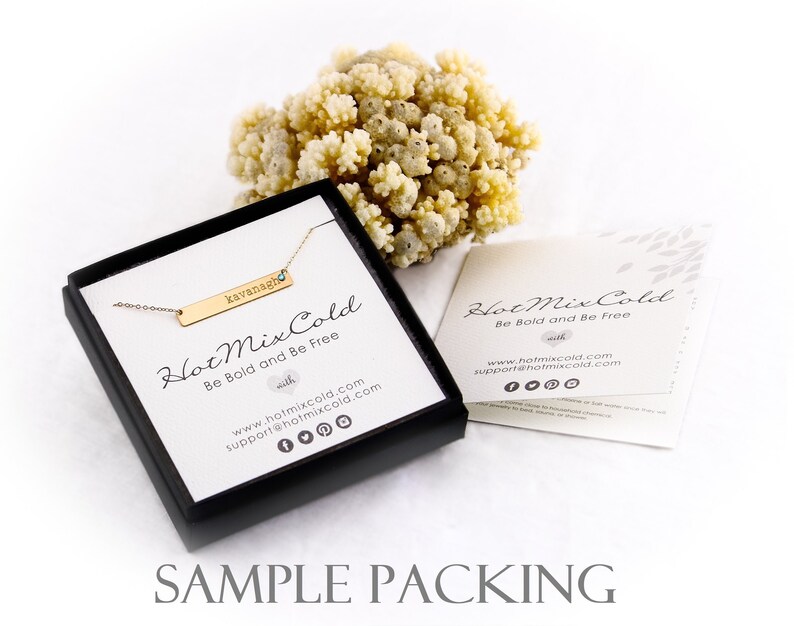 K&ouml;nnte beinhalten: Eine schwarze Schachtel mit einer goldenen Bar-Halskette darin. Die Halskette hat einen kleinen blauen Stein und den Namen "kavanagh" auf der Bar graviert. Die Schachtel tr&auml;gt den Text "Hot Mix Cold Be Bold and Be Free". Die Schachtel steht auf einer wei&szlig;en Oberfl&auml;che.