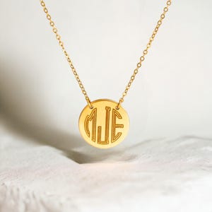 K&ouml;nnte beinhalten: Goldkette mit einem runden Anh&auml;nger, der das Monogramm "MJE" in einer modernen, geometrischen Schriftart tr&auml;gt.