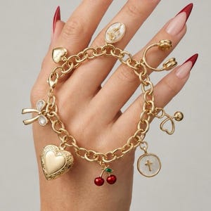 May include: A gold-tone chain link charm bracelet featuring multiple dangling charms including a large heart locket, a pair of red cherries, a white circular cross pendant, a bow, a small heart, and an oval pendant with a floral design.