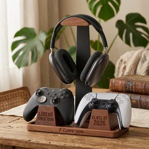 May include: A dark wood and black metal headphone stand with a base tray. The stand holds a pair of black over-ear headphones. Two wooden controller mounts on the base hold a black controller engraved with "LEGEND SINCE 1995" and a white controller engraved with "CLASS OF 2026". The base tray is engraved with "I Love you".