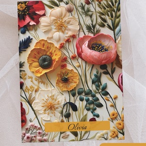 Peut inclure: Une carte à imprimé floral avec un fond blanc et une variété de fleurs dans des tons de rose, rouge, jaune et vert. La carte porte le nom "Olivia" imprimé en lettres dorées en bas. La carte porte également le texte "Golden Beauties" imprimé en lettres dorées en bas.