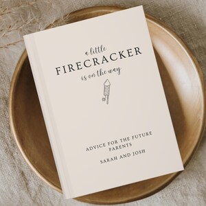 Puede incluir: Un libro blanco con el texto "a little FIRECRACKER is on the way" y una pequeña ilustración de un fuego artificial. Debajo del texto se lee "ADVICE FOR THE FUTURE PARENTS SARAH AND JOSH".