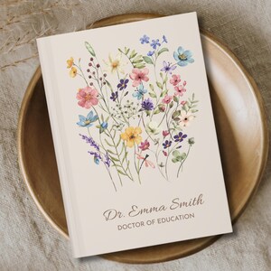 May include: A cream-colored journal with a watercolor floral design featuring pink, blue, yellow, and purple flowers. The cover includes the text "Dr. Emma Smith, Doctor of Education."