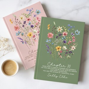 May include: Two hardcover journals, one light pink and one sage green, each featuring a watercolor wildflower bouquet illustration. The green journal displays the text: Chapter 30, Your story is one of courage and kindness, let this new chapter be filled with big dreams and happy adventures, you are the author of a beautiful story, Sally Elke.