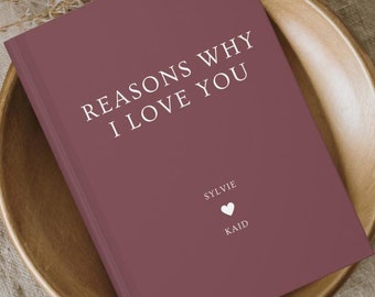Könnte beinhalten: Ein burgunderfarbenes Journal mit dem Text "Reasons Why I Love You" in Weiß. Das Journal trägt die Namen "Sylvie" und "Kaid" in Weiß mit einem weißen Herzsymbol zwischen den Namen.