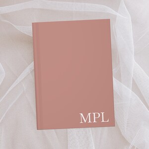 Puede incluir: Un cuaderno de color rosa polvoriento con las letras "MPL" impresas en blanco en la portada.
