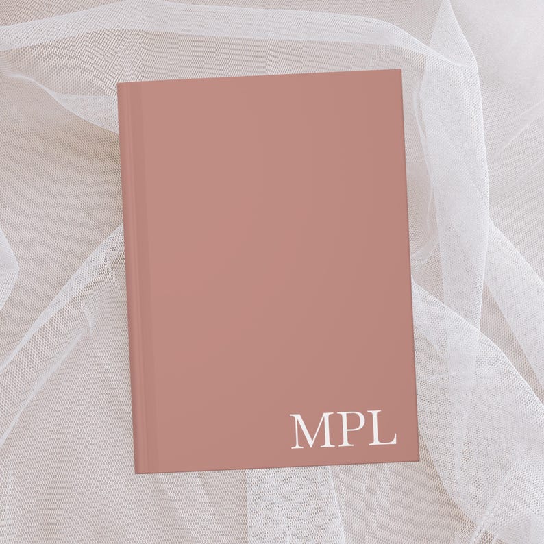 Puede incluir: Un cuaderno de color rosa polvoriento con las letras "MPL" impresas en blanco en la portada.