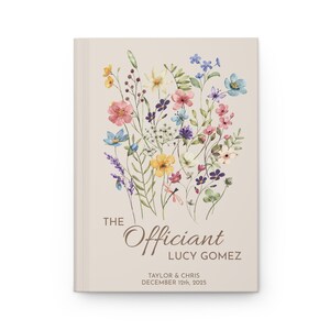 May include: A beige book cover with a floral design in shades of pink, yellow, blue, and green. The text "The Officiant Lucy Gomez" is printed in brown on the cover, along with the names "Taylor & Chris" and the date "December 12th, 2023".