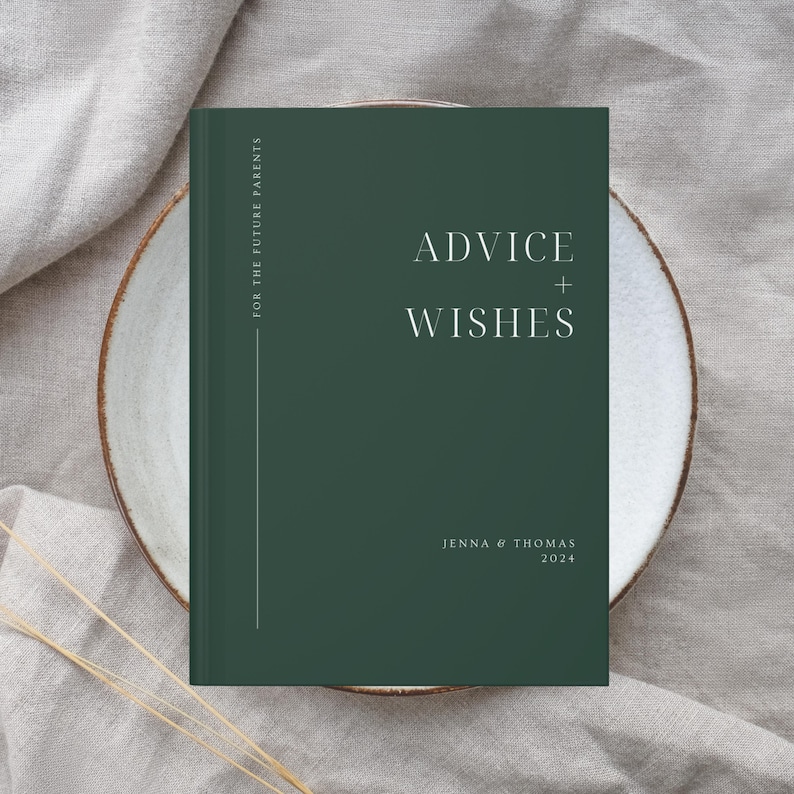 May include: A dark green book with the text "Advice + Wishes" in white on the front cover. The book is on a white plate and has the names "Jenna & Thomas" and the year "2024" printed below the title. The book is titled "For the Future Parents".