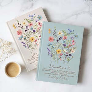 May include: Two hardcover books with floral illustrations on the covers. The blue book features the text "Chapter 70, Your story is one of courage and kindness, Let this new chapter be filled with big dreams and happy adventures, You are the author of a beautiful story, Sally Elke."