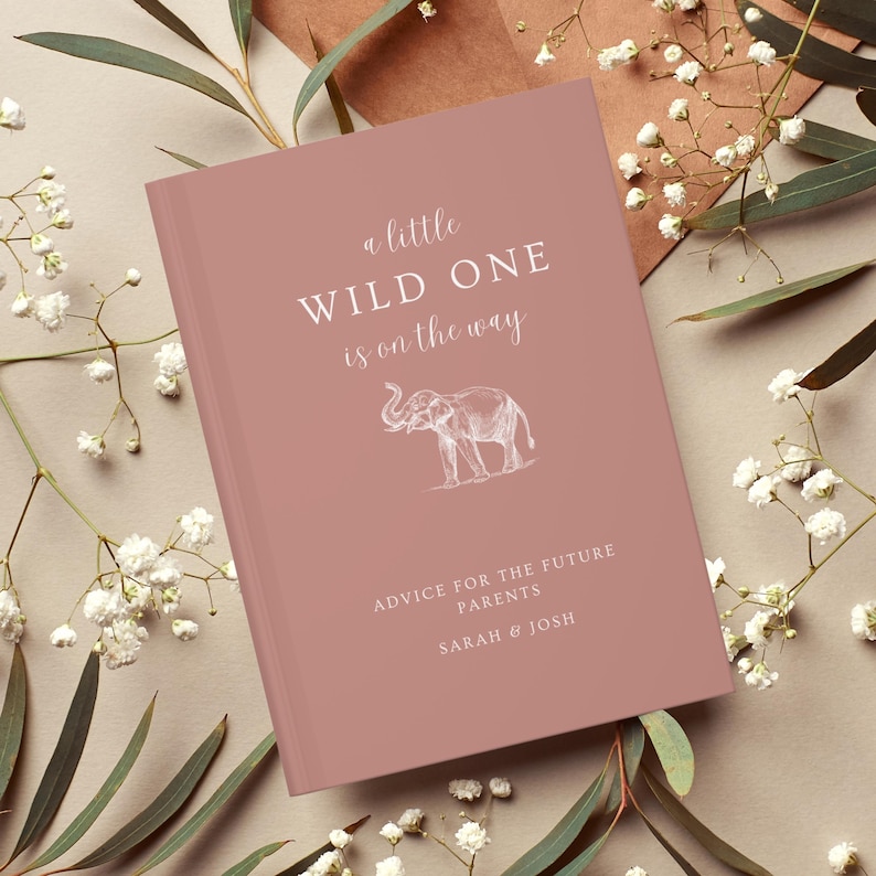 May include: A pink book with the text "a little WILD ONE is on the way" and an illustration of an elephant. The book also has the text "ADVICE FOR THE FUTURE PARENTS SARAH & JOSH".