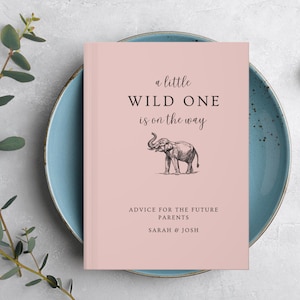 May include: A pink book with the text "a little WILD ONE is on the way" and a black and white illustration of an elephant. The text "ADVICE FOR THE FUTURE PARENTS SARAH & JOSH" is printed below the illustration.