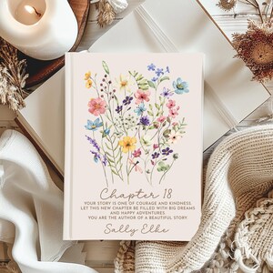 May include: A hardcover book with a light beige cover featuring a watercolor illustration of colorful wildflowers. The text reads: Chapter 18, Your story is one of courage and kindness. Let this new chapter be filled with big dreams and happy adventures. You are the author of a beautiful story. Sally Elke.