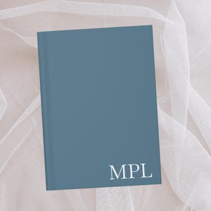 Puede incluir: Un cuaderno de tapa dura azul con las letras "MPL" impresas en blanco en la portada.