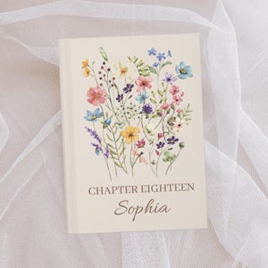 May include: A hardcover book with a cream-colored cover featuring a watercolor floral design in shades of pink, yellow, blue, and purple. The text "CHAPTER EIGHTEEN Sophia" is printed in brown script below the flowers.