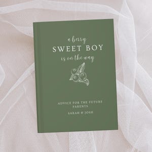 K&ouml;nnte beinhalten: Ein gr&uuml;nes Buch mit dem Text "a berry SWEET BOY is on the way" und einer Illustration von Blaubeeren. Das Buch enth&auml;lt auch den Text "ADVICE FOR THE FUTURE PARENTS" und die Namen "SARAH & JOSH".