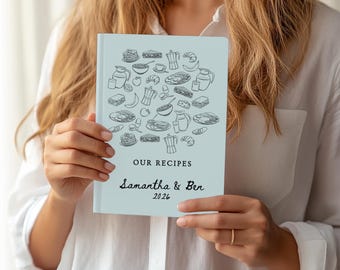 May include: A light blue recipe book with the words "OUR RECIPES" and the names "Samantha & Ben" and the year "2026" in black script. The cover features a black line drawing of various food items.
