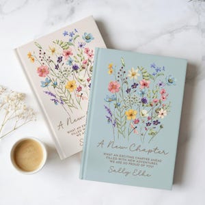 May include: Two hardcover books with floral illustrations on the covers. One book is light blue, the other is cream. Both feature the text A New Chapter, What an exciting chapter ahead filled with new adventures, we are so proud of you, and Sally Elke.
