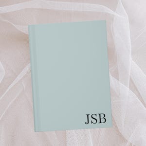 Puede incluir: Un cuaderno azul claro con las iniciales "JSB" impresas en negro en la portada.