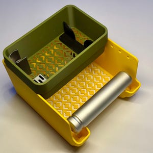 May include: A two-tiered yellow and olive green plastic organizer with a geometric lattice pattern on the base of each section. The top olive green bin contains small dark dividers, while the lower yellow section holds a silver cylindrical tube.